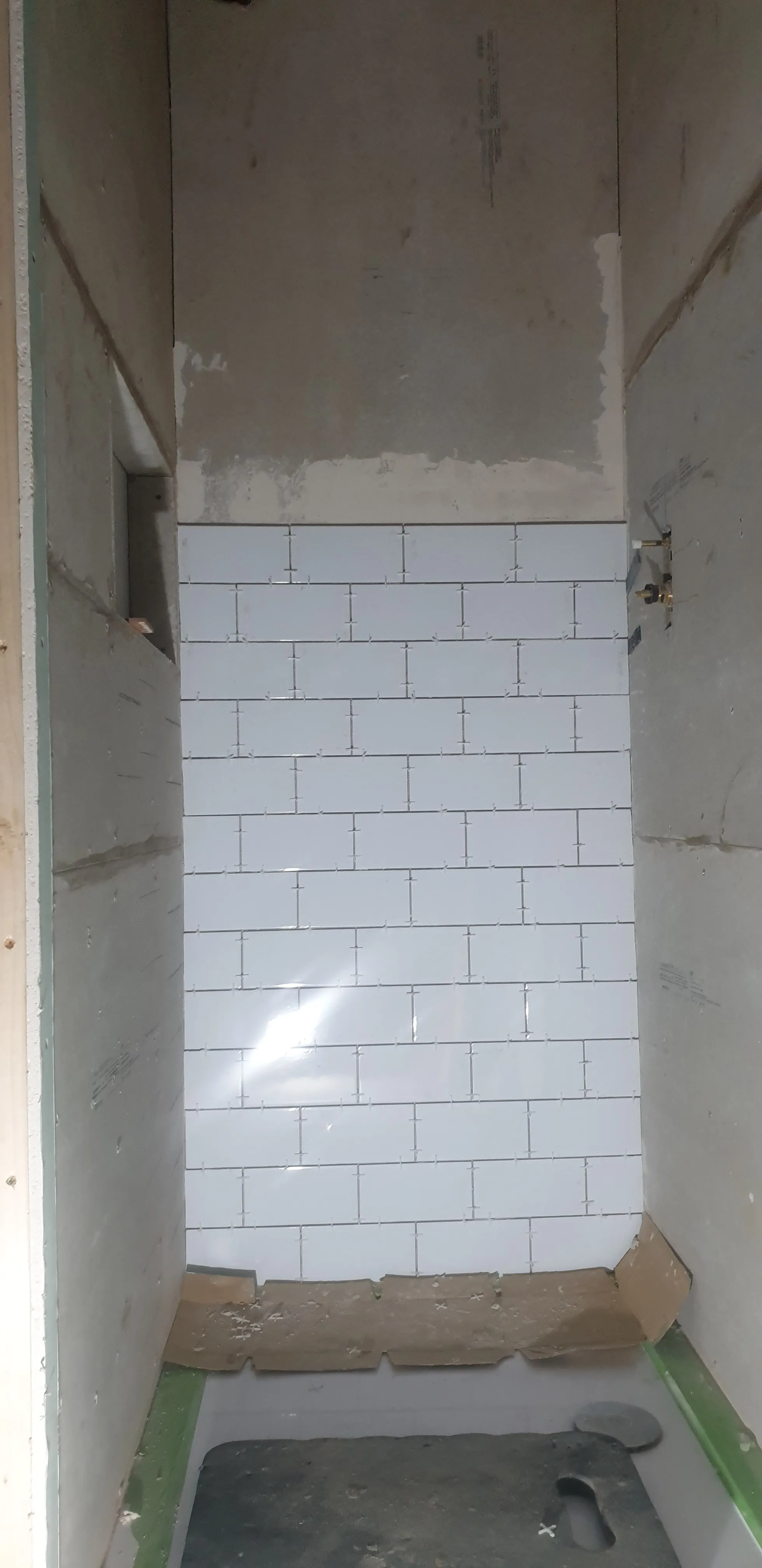 Bathroom during renovation - white metro tiles installation on shower walls